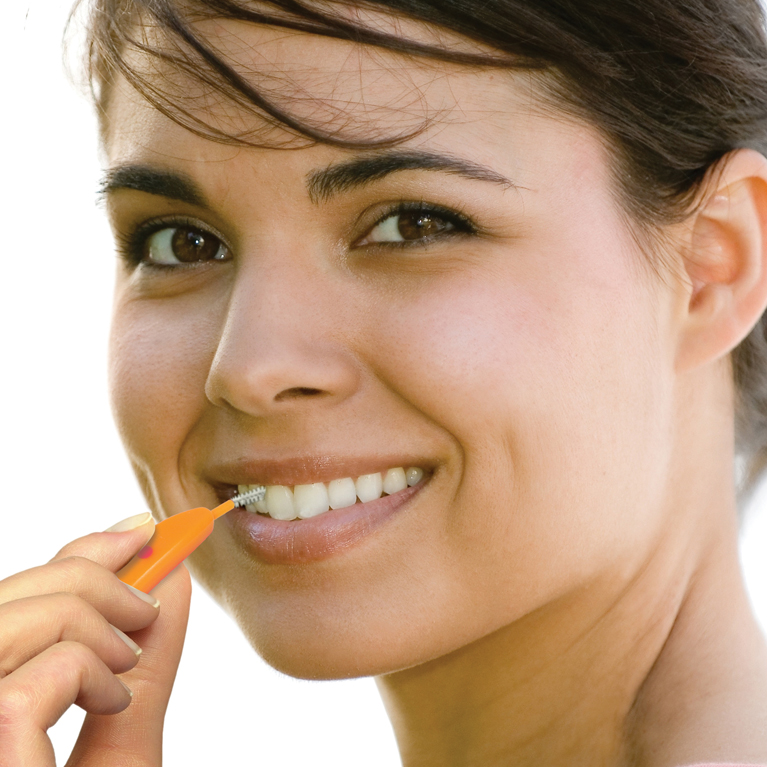 Junge lächelnde Frau putzt ihre Zähne mit der edelwhite Interdentalbürste